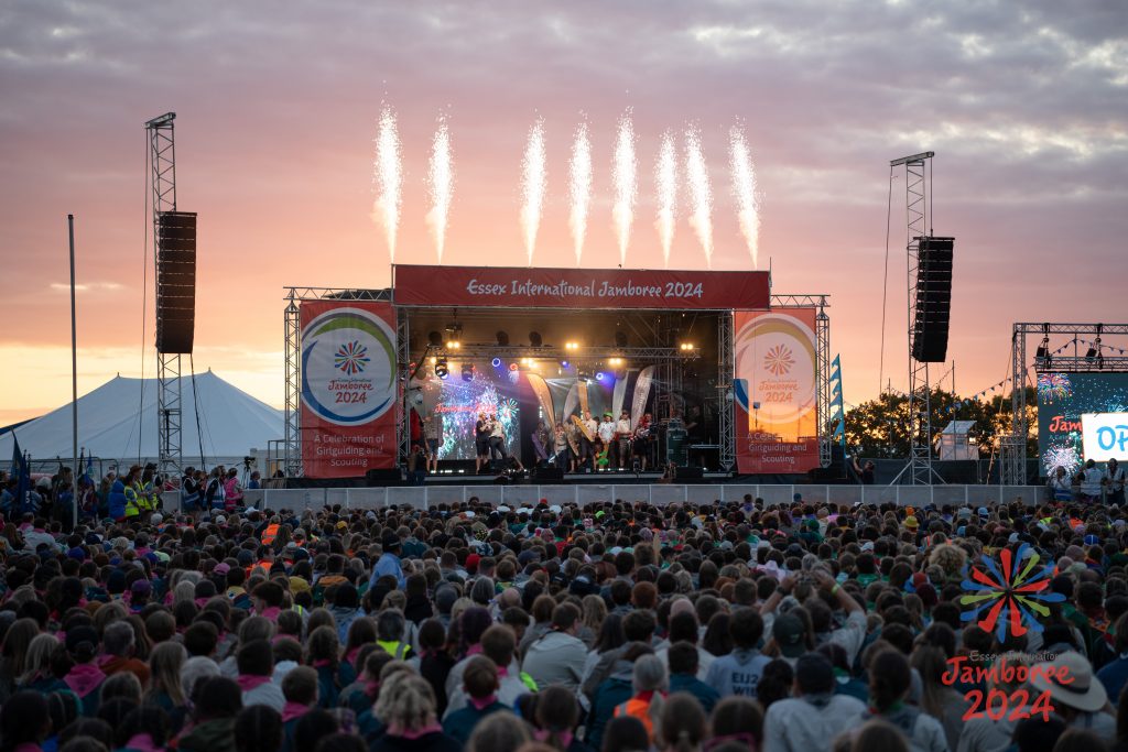 The EIJ 2024 main stage with a sunset in the background. Fireworks are shooting above the stage, while a large crowd watch the action.