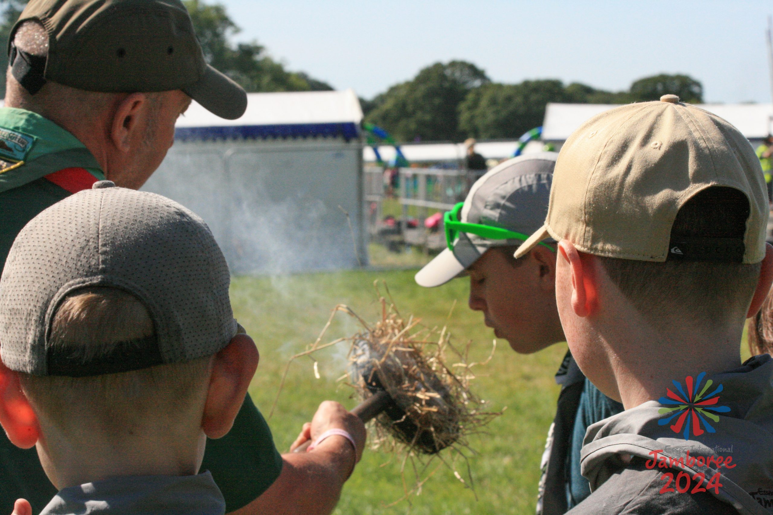 A participant blows on a bundle of straw with a ember starting to smoke