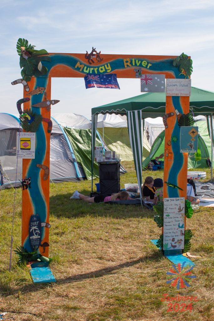 A gateway to a group on Murray subcamp. A painted rendition of the Murray river flows around the arch, with various flags and signs dotted around it. 