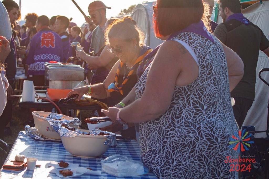 Members of Ganges subcamp serving food to passers by. There's a large crowd surrounding the table. 