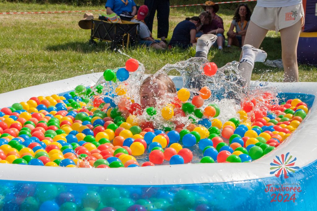 A young person splashing into a paddling pool full of colourful plastic balls.