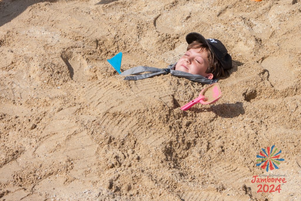 A young person buried in the sand on the EIJ 2024 beach.