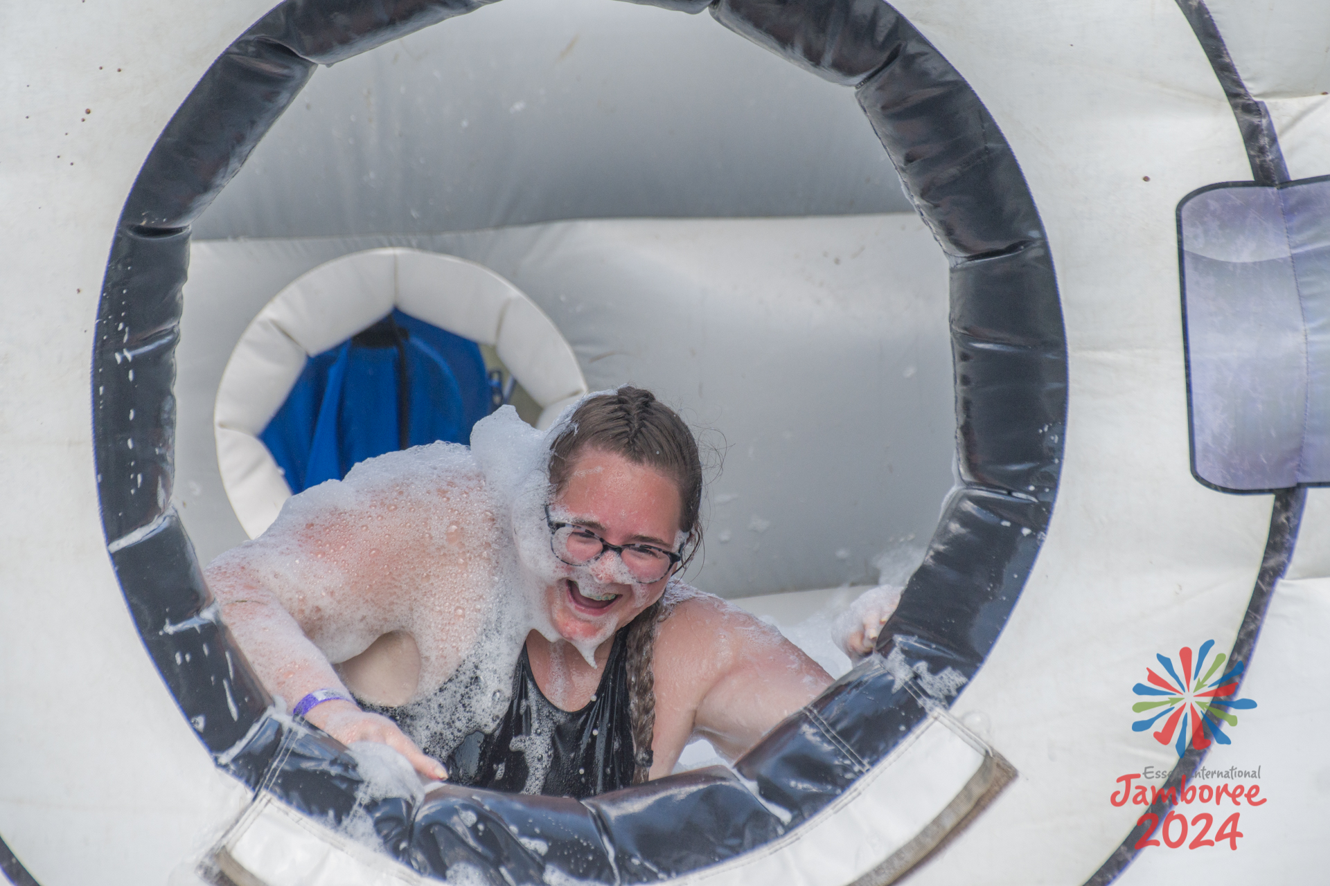 A girl covered in bubbles, climbing out of a giant, inflatable washing machine.