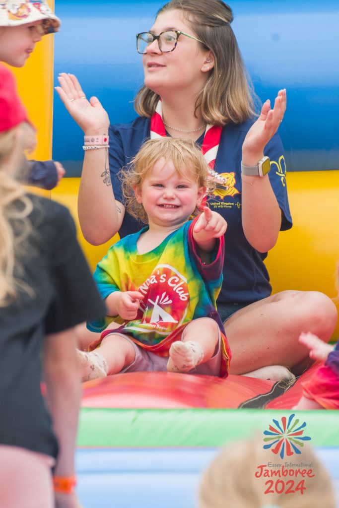 A Noa's Club member sits on a Bouncy Castle and smiles while pointing at the camera