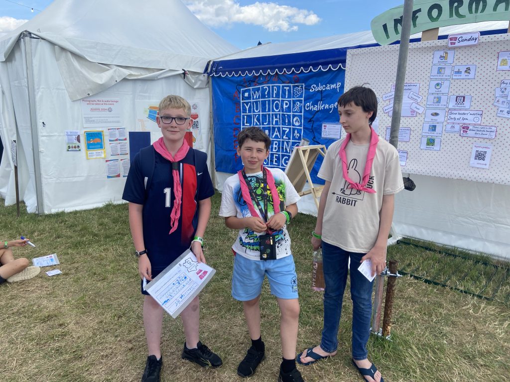 Three young people posing outside the Seine subcamp challenge board. 