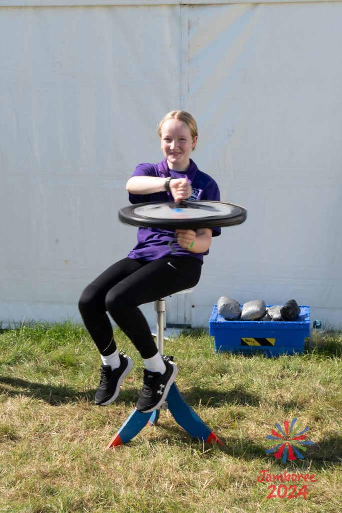 A young person from Ganges subcamp sitting on a stool and holding a spinning bike wheel, in a demonstration of gyroscopic precession.