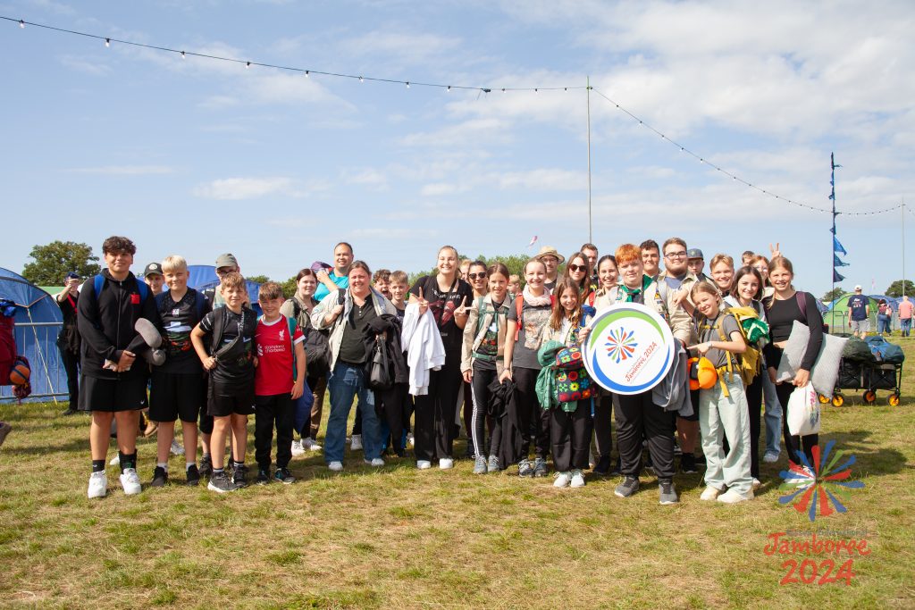 A group photo of the German contingent with all their kit on EIJ way. One of the Scouts at the front is holding a copy of the EIJ 2024 logo.