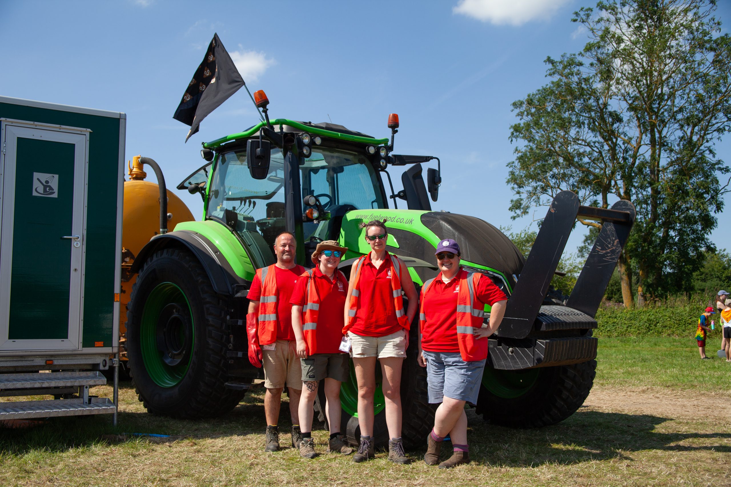 Some EIJ staff in hi-viz jackets in from of a large tractor with a flag featuring poo emojis