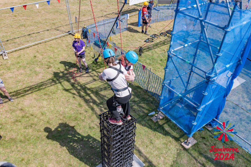 Two girls standing atop a stack of crates, holding onto each other. The photo is taken from above, looking down on the activity.