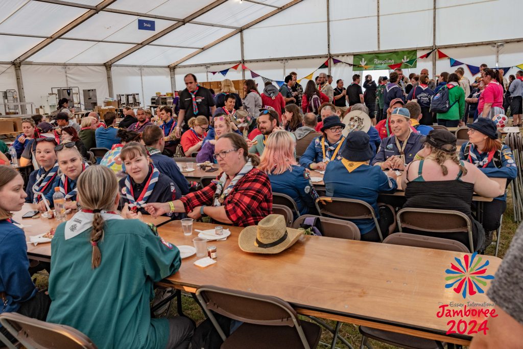 Dozens of Scout and Guide Leaders sit in groups from various countries meet with each other in a marquee tent