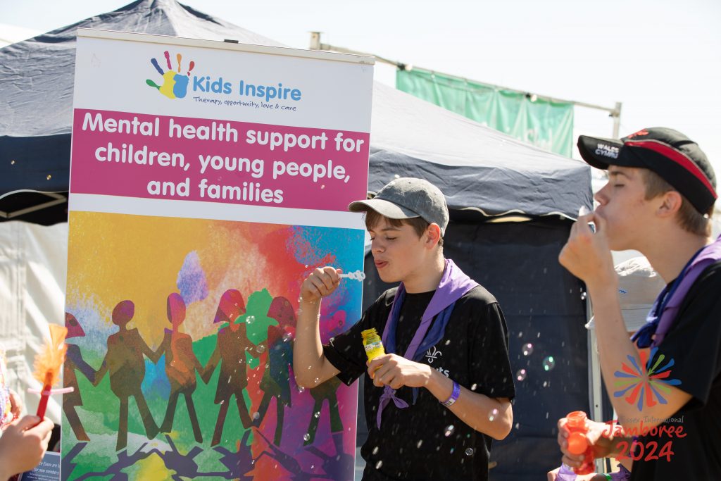 Two Scouts blowing bubbles in front of a Kids Inspire banner.