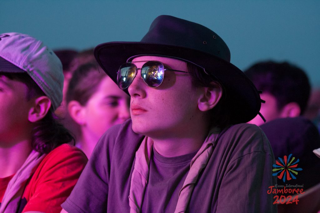 A participant wearing a wide-brimmed hat, watching the action on stage. The stage and the lights are reflecting in his sunglasses.