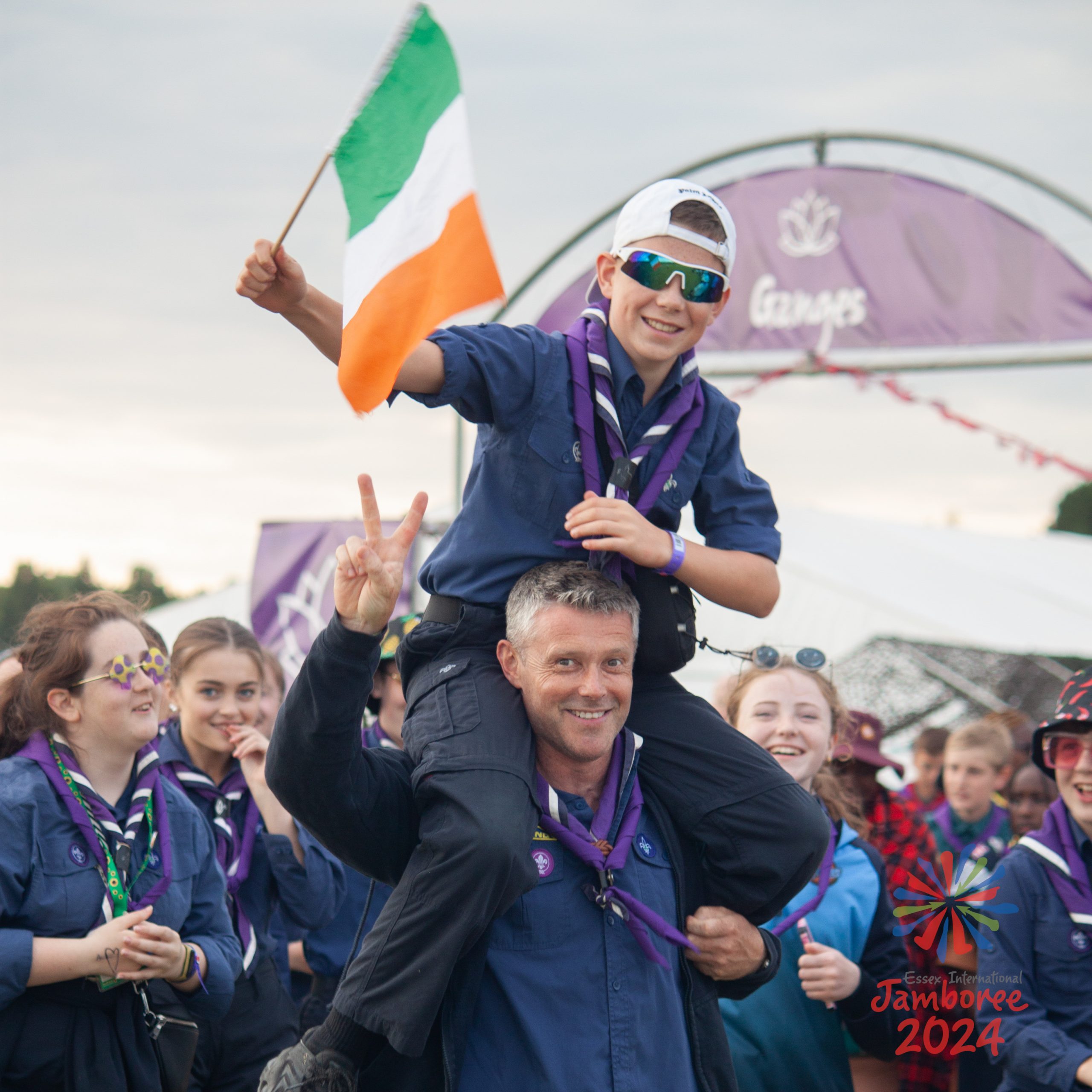 A young person sitting on someone's shoulders, while waving an Irish flag.