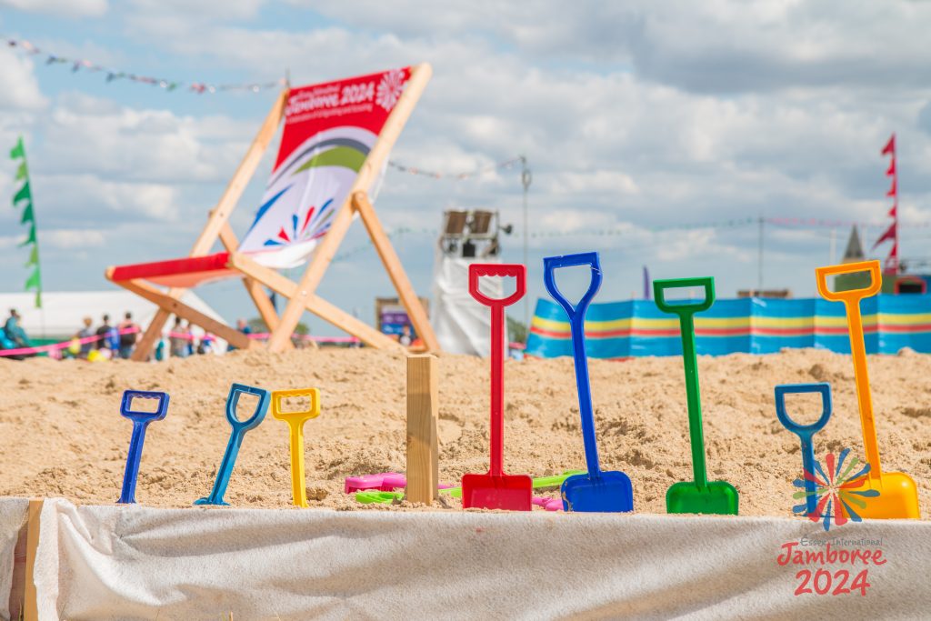 Different coloured spades stuck into the sand in a line. A large EIJ branded deckchair can be seen in the background.