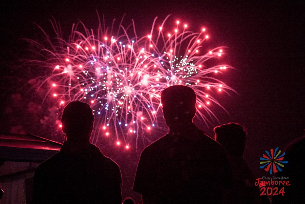 Red fireworks lighting up the sky, partially blocked by the silhouettes of two participants.