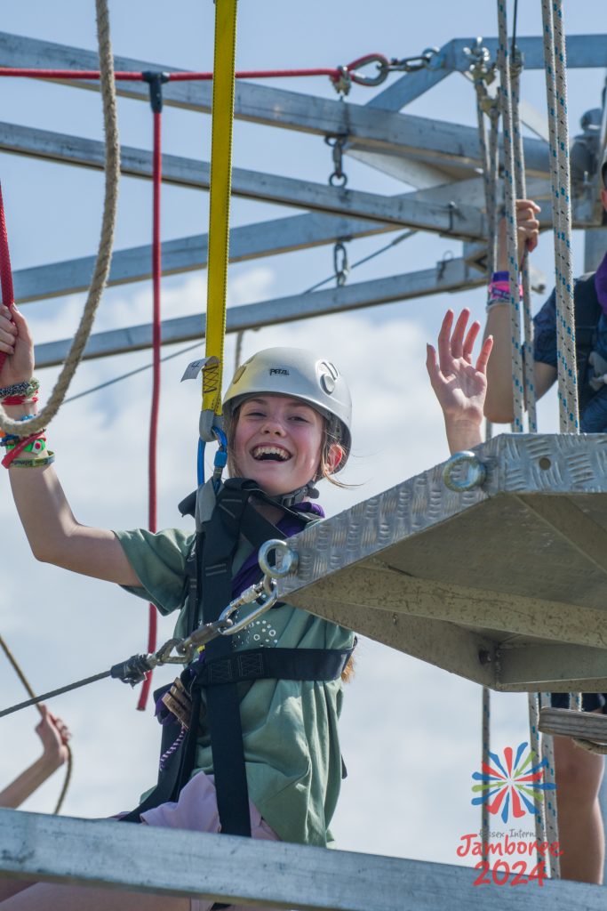 A participant smiles while  tethered to a high-wire course