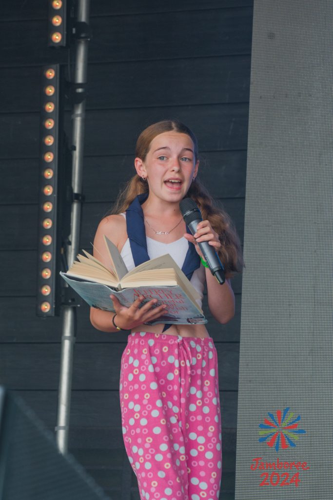 A girl singing into a microphone while holding a large book.