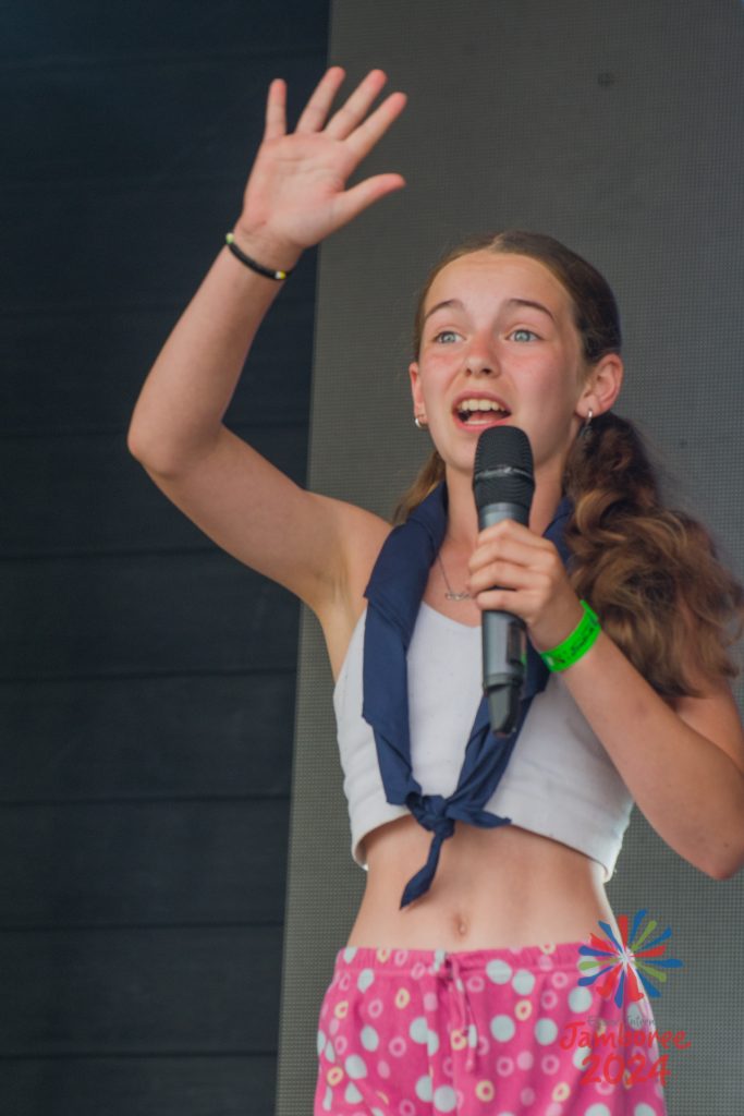 A girl singing into a microphone, with her right hand raised into the air. 