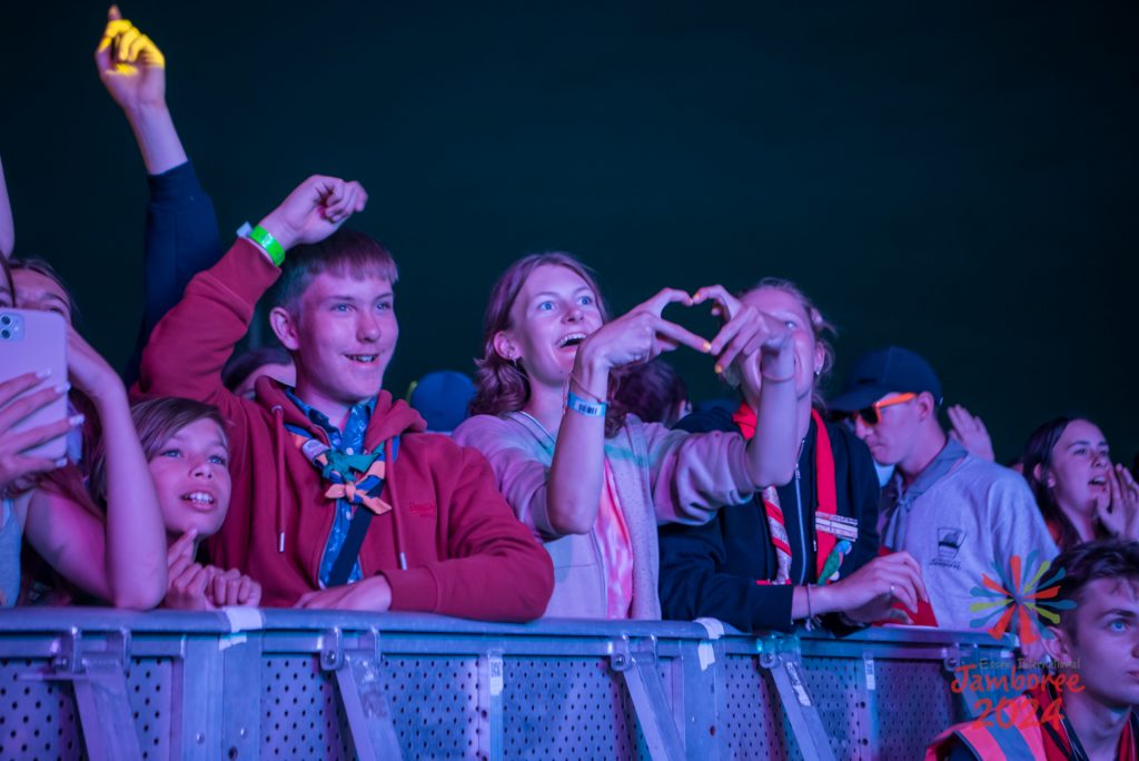 The crowd watching the performers. One girl is forming a heart shape with her fingers.