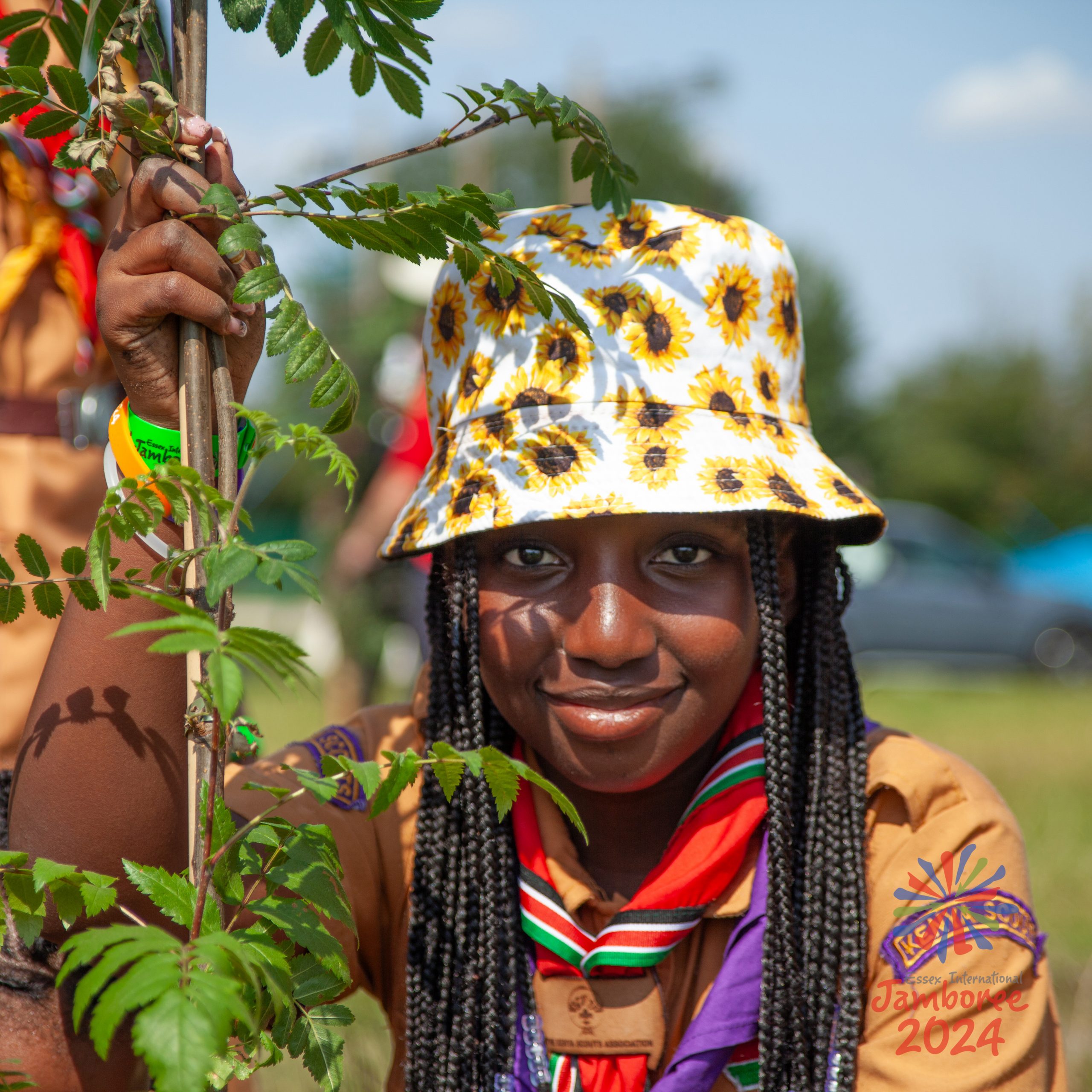 A young person holding a plant, while wearing a bucket hat covered in sunflowers.