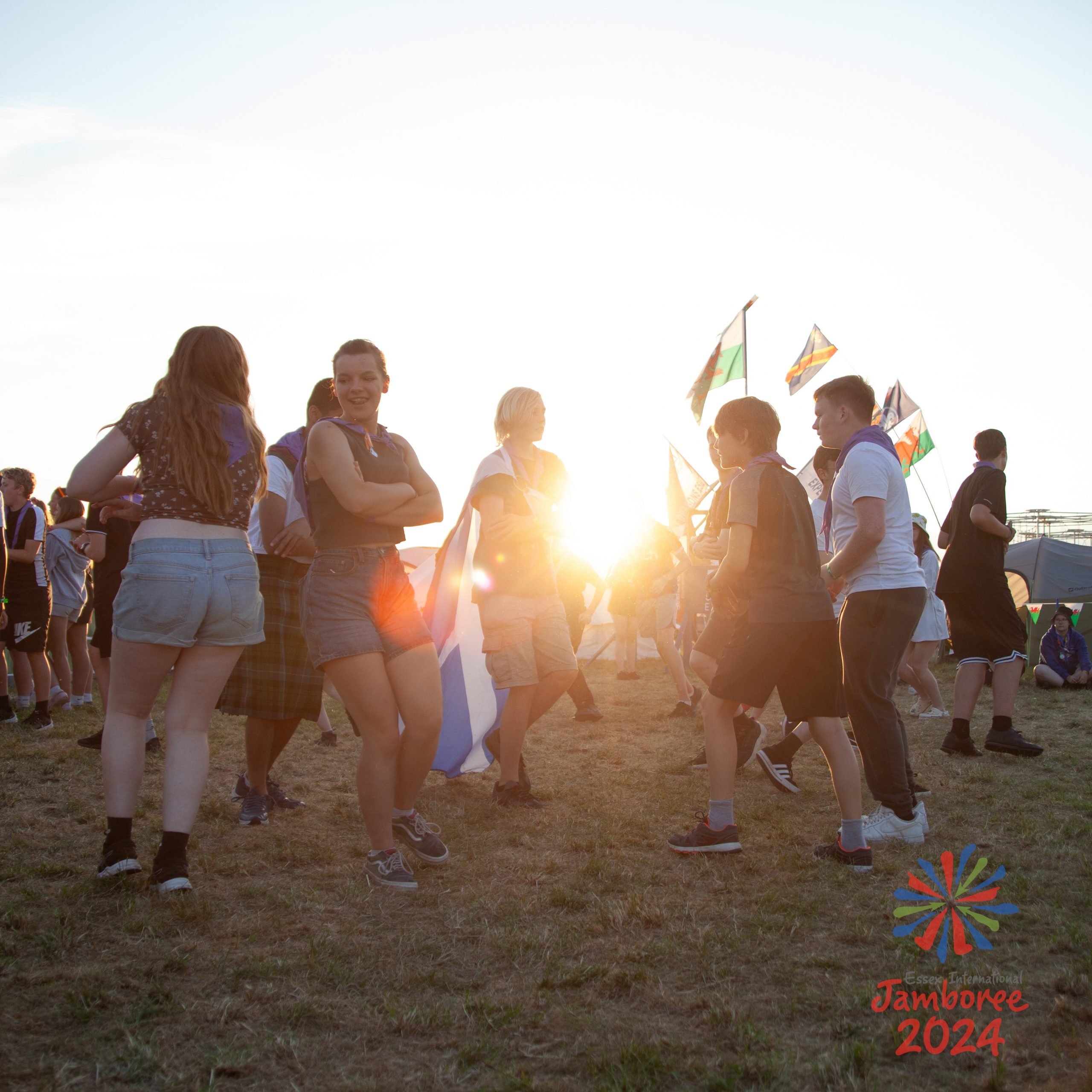 Young people dancing, with the sun setting in the background and shining between them.