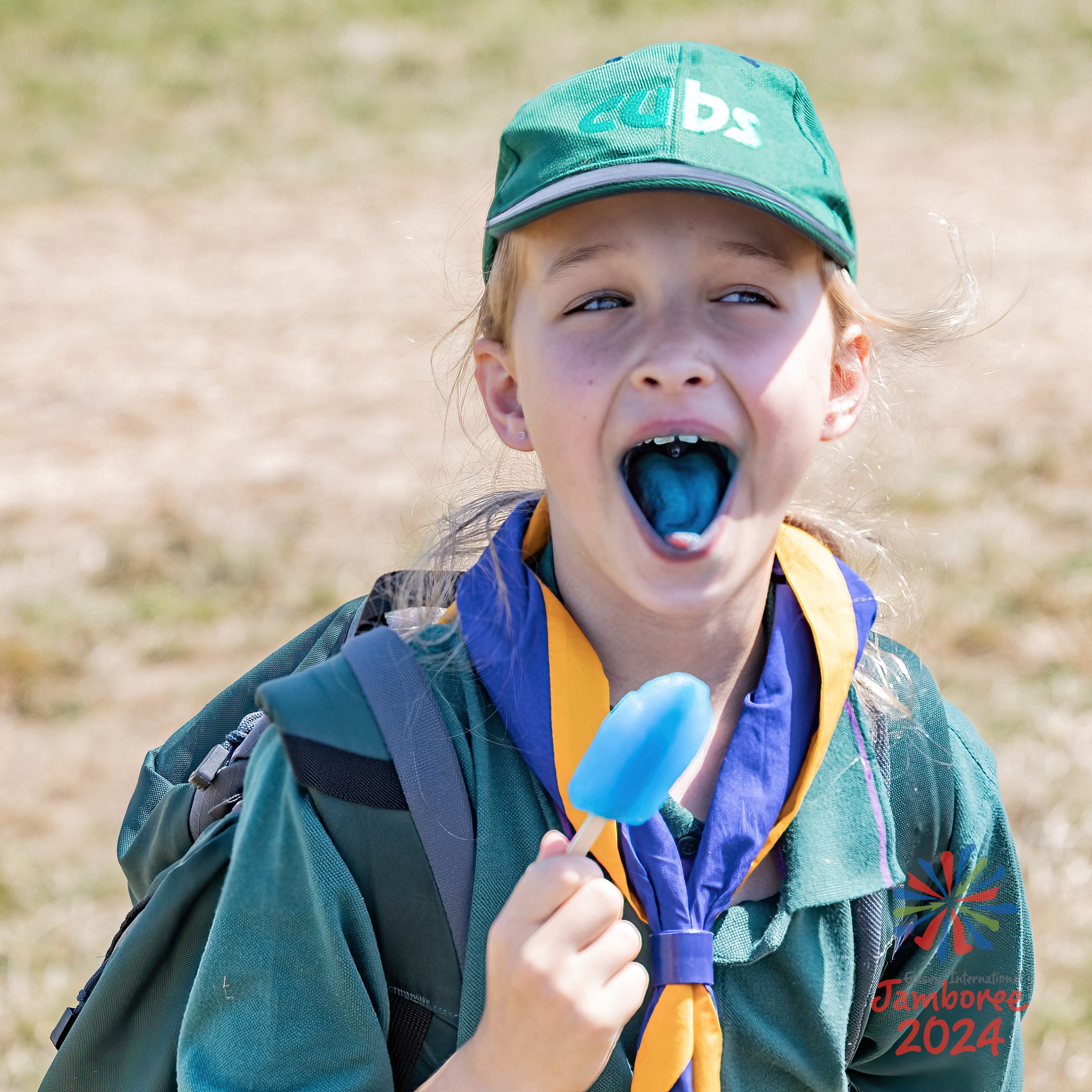 A girl eating a blue ice lolly sticking her tongue out, which is also now blue.